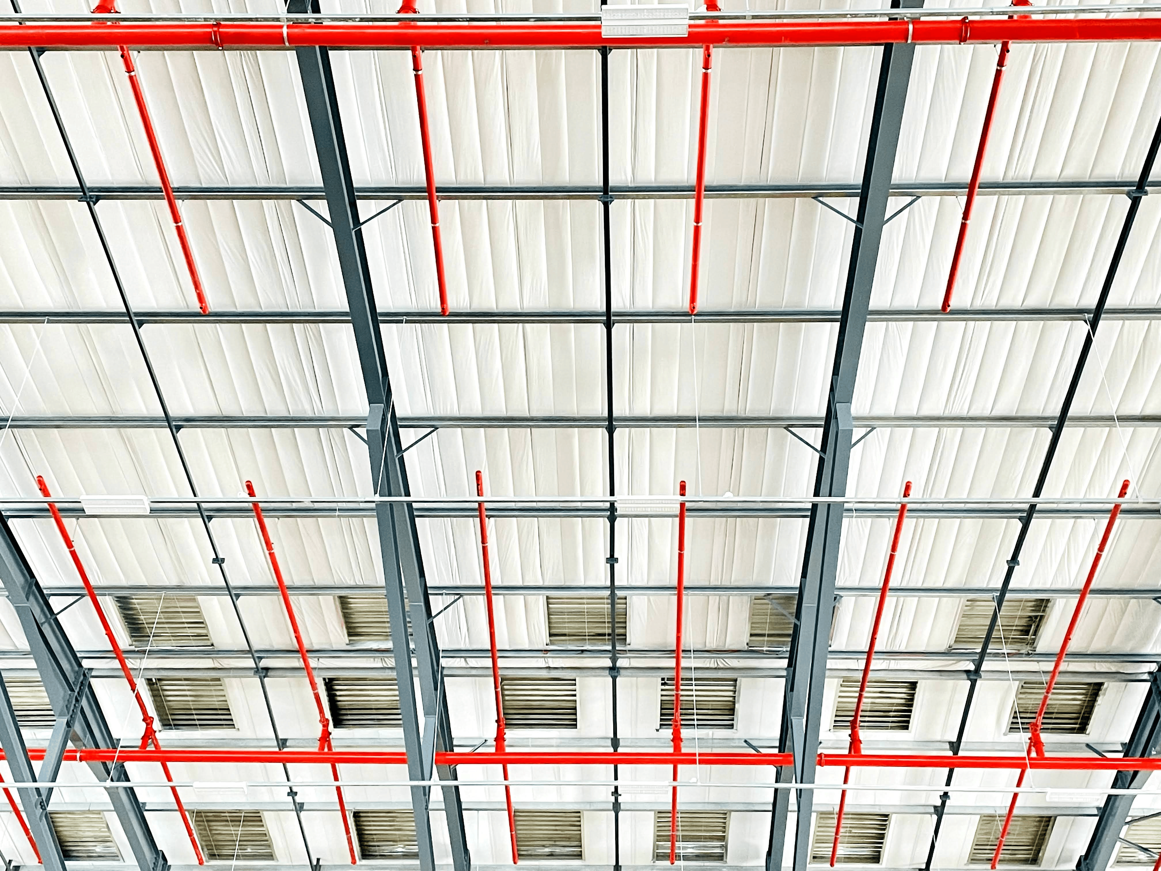 Red sprinkler piping installed beneath an industrial roof